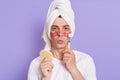 Image of young adult man in towel use eye anti-wrinkle patches, looking at camera with pout lips, doing face massage with roller,