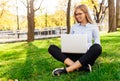 Image of a young amazing lady, sitting in a park, using a laptop computer, sits on a green lawn. Royalty Free Stock Photo