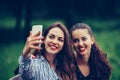 Image of young amazing women friends, students sitting in the park make selfie by mobile phone