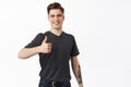 Image of young ambitious guy, college student shows thumb up and smiles satisfied, recommends something and likes