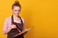 Image of young attentive amateur artist posing with art equipment in both hands, mixing colours, wearing brown apron and striped
