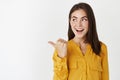 Image of young attractive woman pointing at promo, looking left with excitement and surprise, standing on white Royalty Free Stock Photo