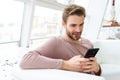 Image of young bearded man using smartphone while sitting in cafe indoors Royalty Free Stock Photo