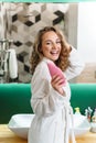 Image of young woman in housecoat holding body lotion after shower