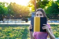 Image of young beautiful girl hiding behind the book in the summer park Royalty Free Stock Photo