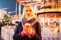 Image of young blonde with glass in hands on background of carousel in evening for walk Royalty Free Stock Photo