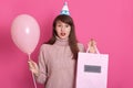 Image of young darkhaired teenage girl holding balloon and packadge with present, dresses pink sweater and bithday hat, female Royalty Free Stock Photo