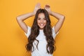 Image of young european woman 20s with long hair smiling and showing rabbit ears at her head, isolated over yellow background Royalty Free Stock Photo