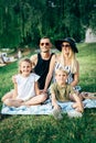 Image of young family with children sitting on plaid on picnic on summer day