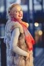 Image of young fashionable blonde in fur vest on walk in city in evening. Royalty Free Stock Photo