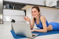 Image of young fitness girl talking online on laptop, video chats, laying on floor rubber mat, doing exercises, discuss Royalty Free Stock Photo