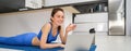 Image of young fitness girl talking online on laptop, video chats, laying on floor rubber mat, doing exercises, discuss Royalty Free Stock Photo