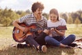 Image of young handsome man with dark curly hair teaches playing guitar her friend, couple have picnic in meadow, have romantic, Royalty Free Stock Photo