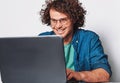 Image of young happy businessman with curly hair working on his laptop in office. Cheerful smiling student man sitting at his desk Royalty Free Stock Photo