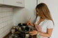 Image of young happy lady standing in kitchen while cooking fish. Looking at camera. Royalty Free Stock Photo