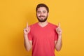 Image of young happy man with good mood, posing isolated over yellow background, pointing up with his index fingers, looking Royalty Free Stock Photo