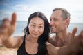 Young happy white man kissing and hugging beautiful asian woman while taking selfie photo on sunny beach Royalty Free Stock Photo