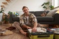 Image of young man, traveller, sitting on floor with opened suitcase, packing clothes for a trip, going on holiday Royalty Free Stock Photo