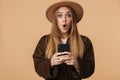 Image of young optimistic girl wearing hat wondering and holding cellphone