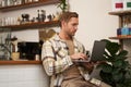 Image of young stylish guy with laptop, sitting in cafe with his computer, typing something, drinking coffee and doing Royalty Free Stock Photo