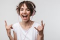 Image of young woman in basic t-shirt showing rock sign while listening to music with headphones Royalty Free Stock Photo