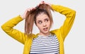 Image of young woman collecting hair in a ponytail, wearing casual outfit, posing over white studio wall. Female makes ponytail,