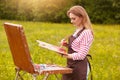 Image of young woman drawing picture on canvas, using sketchbook for drawing in nature, painter girl profile with brush and