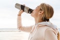 Image of young woman drinking water from bottle while working out on pier near seaside in morning Royalty Free Stock Photo