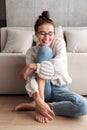 Image of young woman in eyeglasses smiling and sitting on floor at home Royalty Free Stock Photo