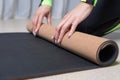 Image of a young woman in a gymnastics suit rolling up a mat after a workout. The concept of fitness, yoga, pilates