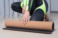 Image of a young woman in a gymnastics suit rolling up a mat after a workout. The concept of fitness, yoga, pilates