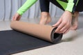 Image of a young woman in a gymnastics suit rolling up a mat after a workout. The concept of fitness, yoga, pilates