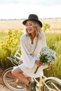 Image of young woman holding flowers and riding bicycle in countryside Royalty Free Stock Photo