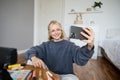 Image of young woman, vlogger taking selfie in her room, talking to her followers during online live stream, using Royalty Free Stock Photo