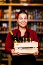 Image of young woman with wooden box with bottles in her hands in wine shop
