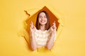 Imaged of smiling happy brunette woman stands in torn paper hole, standing with crosses fingers, posing with closed eyes, hope, Royalty Free Stock Photo