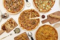 Imagen top view of a white table with pizzas of various flavors sliced with bacon, mushrooms, cheese, sauces, zucchini, tomato and