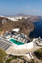 Guests at a hotel pool in Imerovigli overlooking the high cliffs and village of Fira, Santorini, Greece