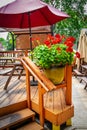 IMG_0204 copy.psdPot of red geraniums sitting on wooden deck with picnic tables and umbrellas in leafy neighborhood - resturant Royalty Free Stock Photo