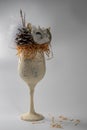A textured, cream-colored goblet decorated with a pine cone, white artificial flower, and fluffy white feathers. Royalty Free Stock Photo
