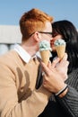 Immersed couple sitting outdoors, holding ice cream, sensually kissing