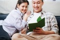 Immersed young couple sitting on a sofa, reading a book together. Royalty Free Stock Photo
