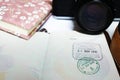 Immigration stamp on a passport. Blurred background of camera and notebook. Travelling concept. Royalty Free Stock Photo