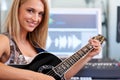 Immortalizing her music. A beautiful blonde guitarist sitting in a recording studio with her instrument - portrait. Royalty Free Stock Photo