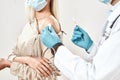 Immunisation. Cropped close up shot of male doctor in blue sterile gloves injecting vaccine to a young woman wearing