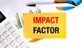 Impact factor phrase on yellow card with calculator, charts and pen on white office desk Royalty Free Stock Photo