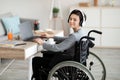 Impaired teenager in wheelchair studying online with laptop, using headphones for remote communication at home, mockup Royalty Free Stock Photo