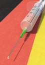 A syringe with vaccine lies on a german flag, portrait format