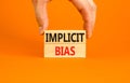 Implicit bias symbol. Concept words Implicit bias on wooden block. Beautiful orange table orange background. Businessman hand.