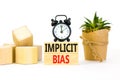 Implicit bias symbol. Concept words Implicit bias on wooden block. Beautiful white table white background. Black alarm clock.